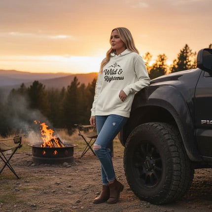 Woman wearing Wild & Righteous hoodie at sunset campfire with truck in mountain setting